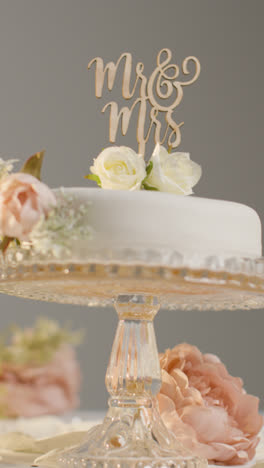 Vertical-Video-Close-Up-Of-Wedding-Cake-On-Stand-Against-Grey-Studio-Background-At-Wedding-Reception